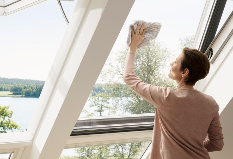 Une femme nettoie la fenêtre de toit VELUX de son séjour de l'intérieur.