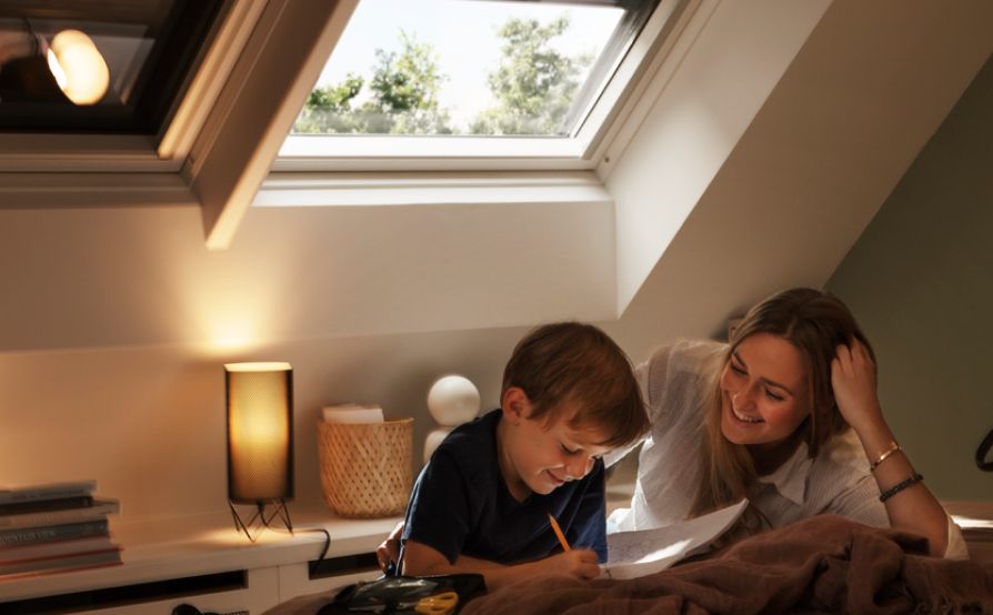 Junge liest seiner Mutter in seinem Schlafzimmer aus einem Buch vor, mit zwei VELUX Dachfenstern im Hintergrund, mit Verdunkelungsrollos.