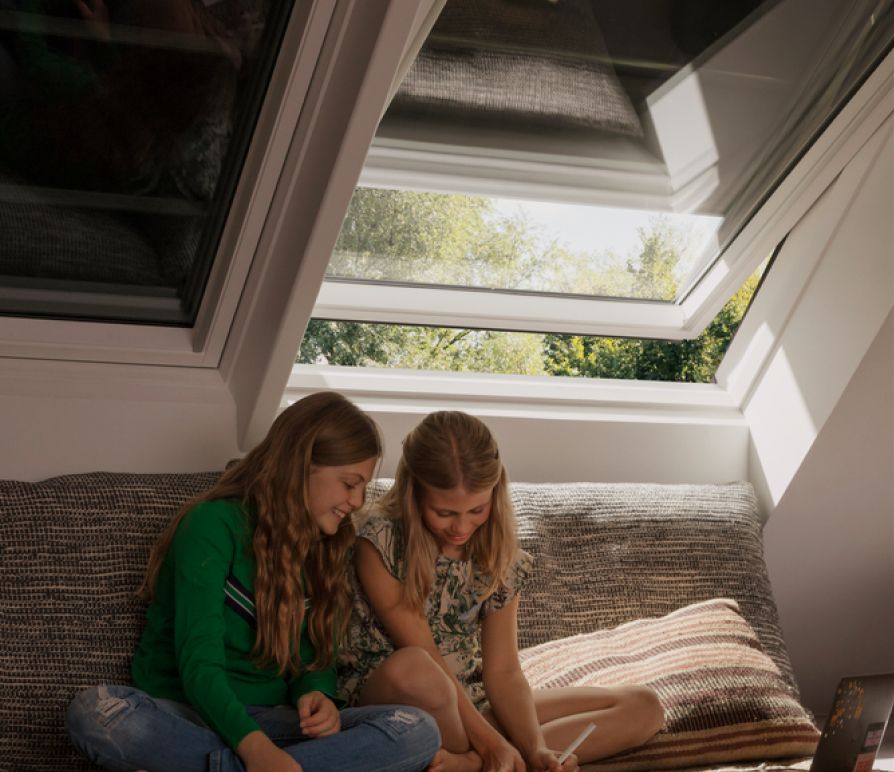 Zwei Mädchen sitzen in einem Kinderzimmer mit zwei VELUX Dachfenstern mit VELUX Verdunkelungsrollos im Hintergrund.