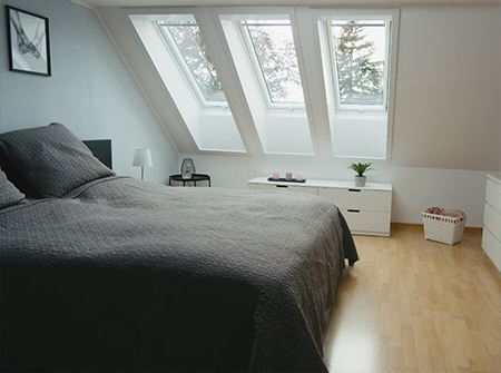 Ein Schlafzimmer mit dunkler Ausstattung und drei langen VELUX Dachfenstern