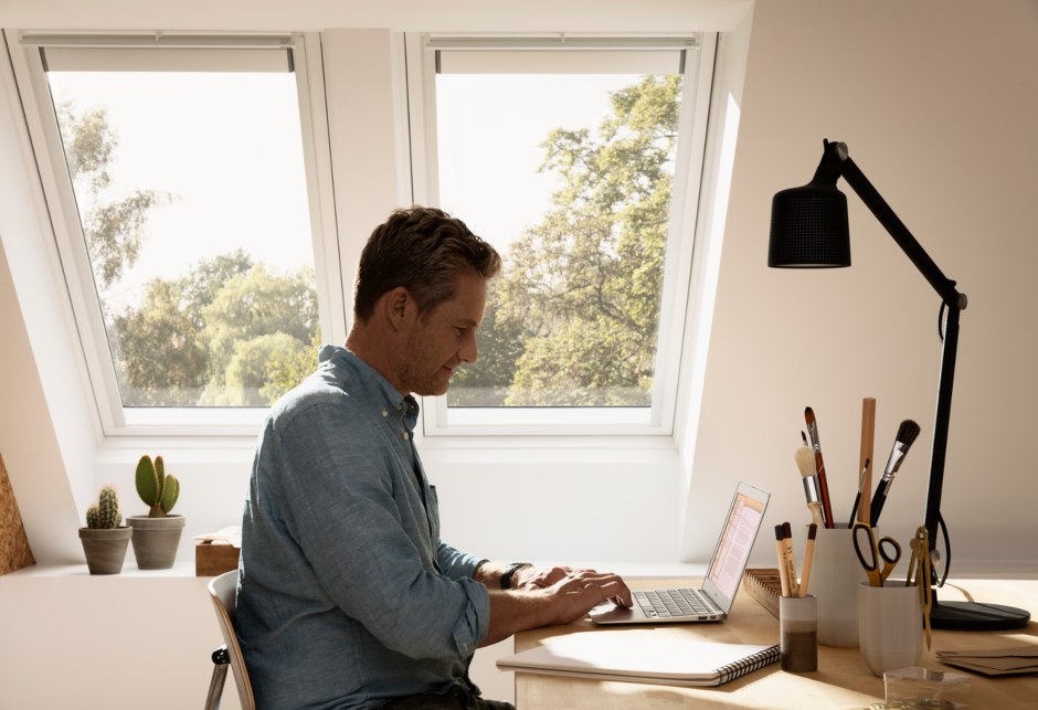 Mann an seinem Schreibtisch sitzend, im Hintergrund zwei VELUX Dachfenster.