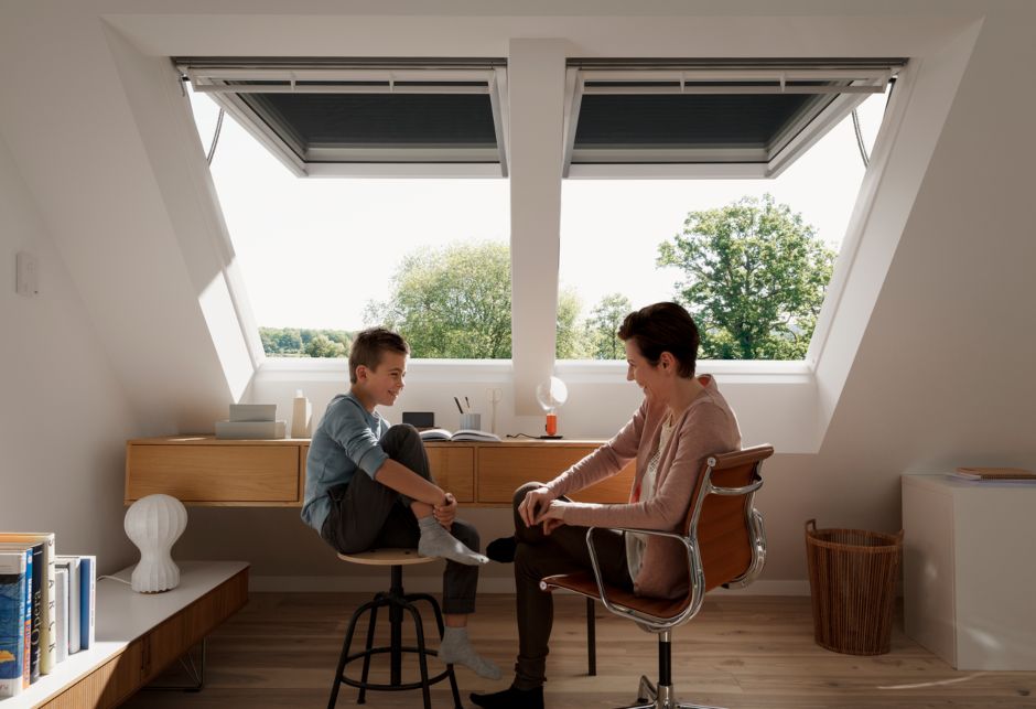 Eine Frau und ein Junge unterhalten sich vor zwei VELUX Klapp-Schwingfenstern sitzend.