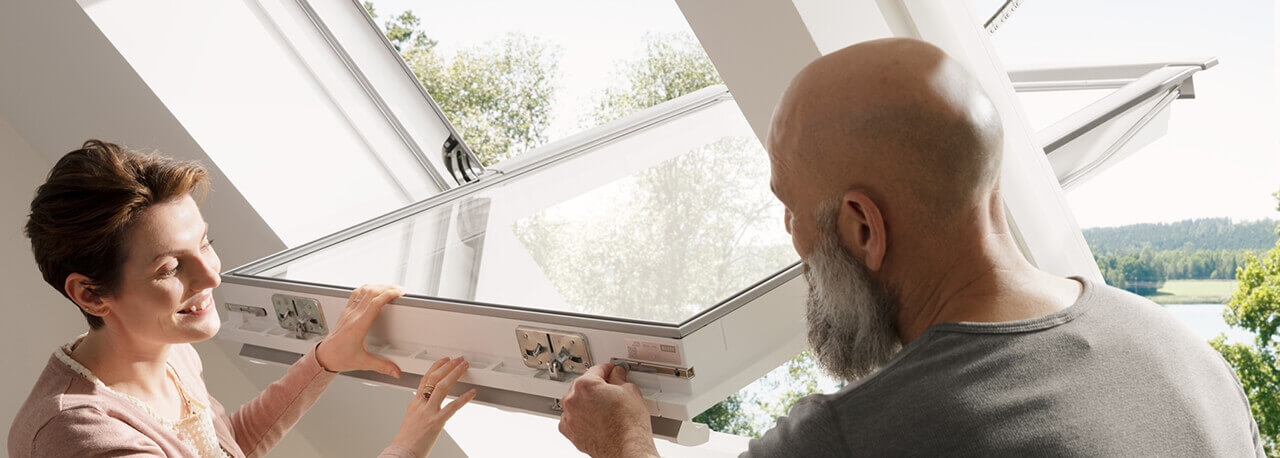 Ein Mann und eine Frau betrachten die Fensterbedienfunktion eines VELUX Dachfensters.