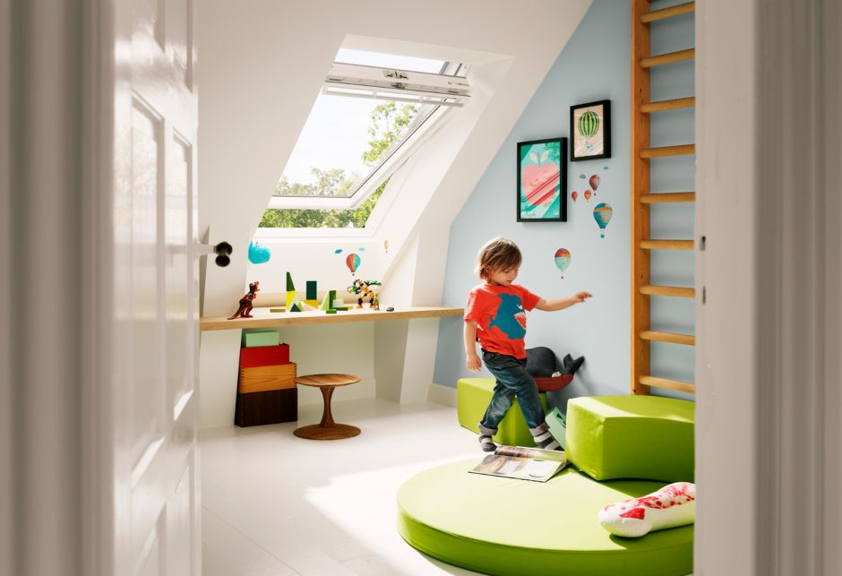 Ein kleiner Junge spielt in einem farbenfrohen Raum, hinter ihm befindet sich ein großes VELUX Dachfenster.