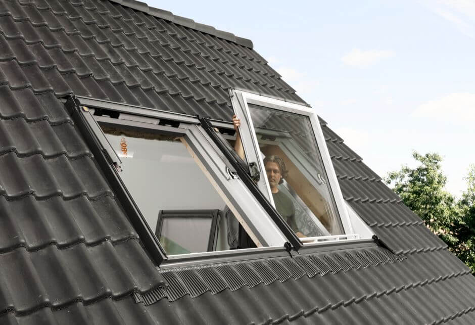 A male installer positions one of two VELUX roof windows in a black roof.