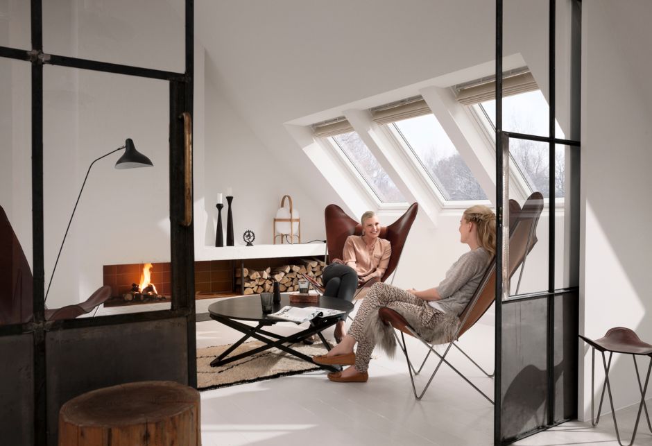 Two women sit on chairs in a living room, there are three VELUX roof windows behind them.